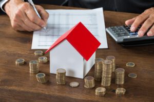 Property investor makes calculations in front of wooden house and stacks of coins