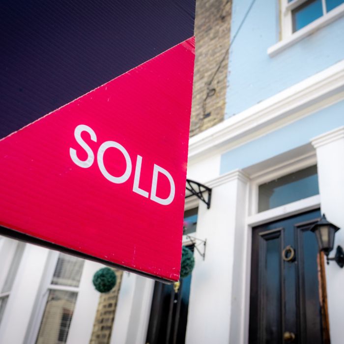 Estate agent sold sign with houses in background